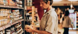 Man looking at a jar of peanut butter with a label on it.