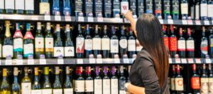 lady grabbing wine bottle from wine aisle